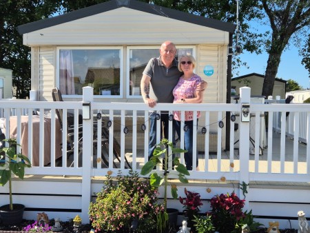 David Cope wraps his arm around his wife Julie outside their caravan in North Wales, the pair have huge smiles on their face knowing they can spend more time here in the summer as his condition has improved.